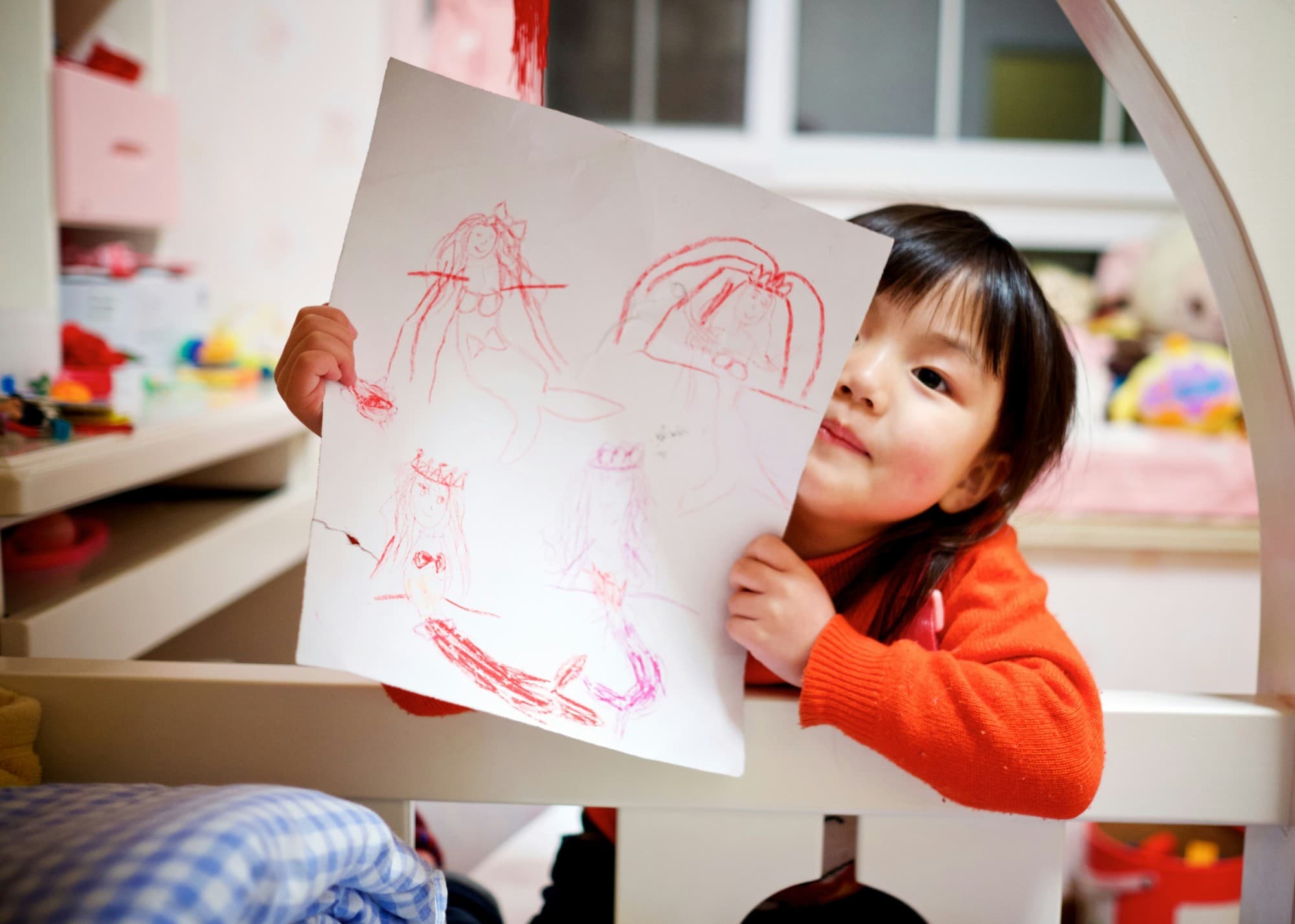 A young child proudly holding up a drawing she made